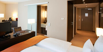 Modern hotel room at the ATLANTIC Grand Hotel Bremen with double bed, desk, TV and open bathroom.