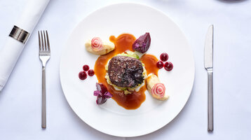 Gourmetgericht auf weißem Teller: Steak mit Sauce, Beilagen und Dekoration, auf weißer Tischdecke angerichtet.