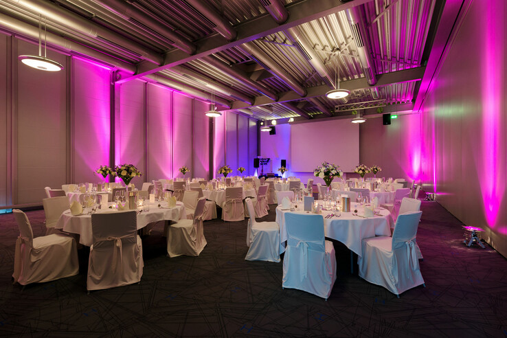 Modern banquet hall in the ATLANTIC Hotel Universum, Bremen, with round tables, white chairs and pink lighting.