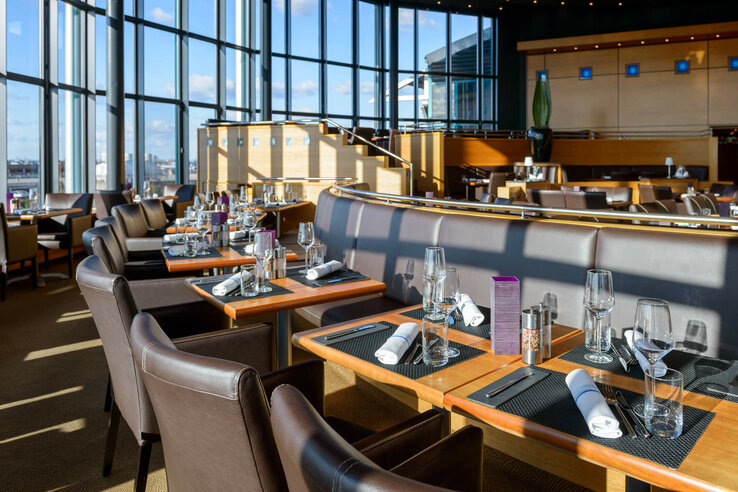 Modern restaurant in the ATLANTIC Hotel Airport Bremen with elegant table settings, large windows and a view of the airport.