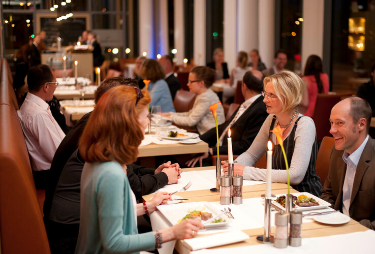Gäste im eleganten Restaurant des ATLANTIC Hotel Kiel, bei Kerzenschein speisend.