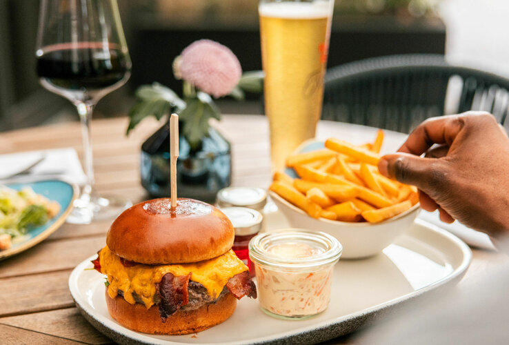 Bild eines Cheeseburgers mit Pommes und amerikanischem Krautsalat, dazu ein Glas Bier und Rotwein