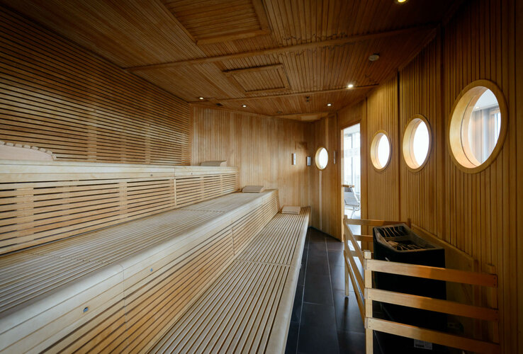 Helle Holzsauna im ATLANTIC Hotel Sail City mit runden Fenstern und mehreren Sitzstufen.