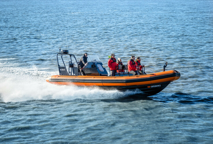 Ein oranges Schnellboot mit Passagieren fährt über das Wasser.