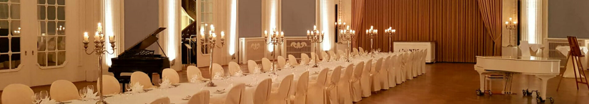 Eleganter Festsaal mit langem, gedecktem Tisch, Kronleuchter und Flügel im ATLANTIC Grand Hotel Travemünde.