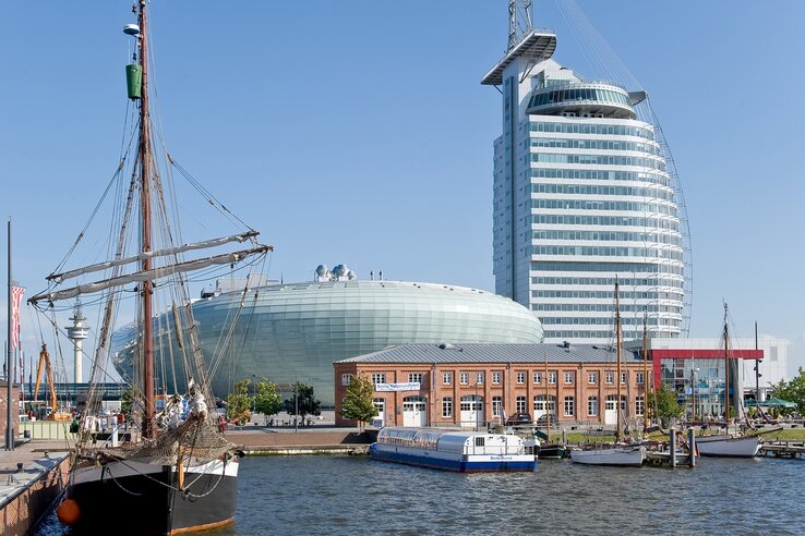 Harbor view with sailing ship, modern glass building and historic brick building under a clear sky.