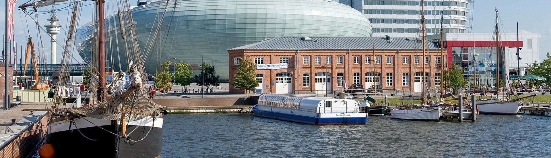 Harbor view with sailing ship, modern glass building and historic brick building under a clear sky.
