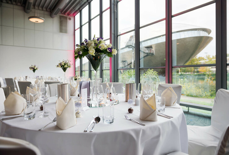 Eleganter Bankettsaal im ATLANTIC Hotel Universum mit gedeckten Tischen und Blick auf moderne Architektur durch große Fenster.