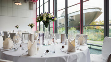 Hochzeit mit Blick auf das Universum Bremen Eleganter Bankettsaal im ATLANTIC Hotel Universum mit gedeckten Tischen und Blick auf moderne Architektur durch große Fenster.