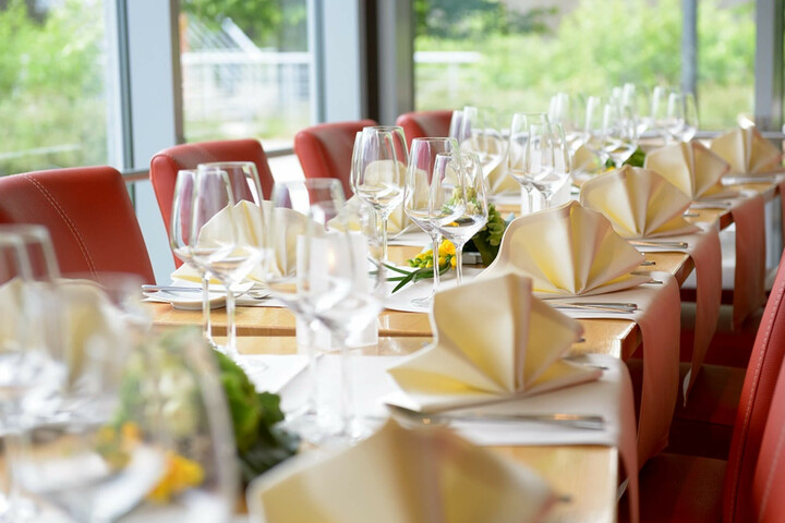 Restaurant CAMPUS Bremen Elegante, gedeckte Tafel im ATLANTIC Hotel Universum mit roten Stühlen, weißen Servietten und Weingläsern vor großen Fenstern.