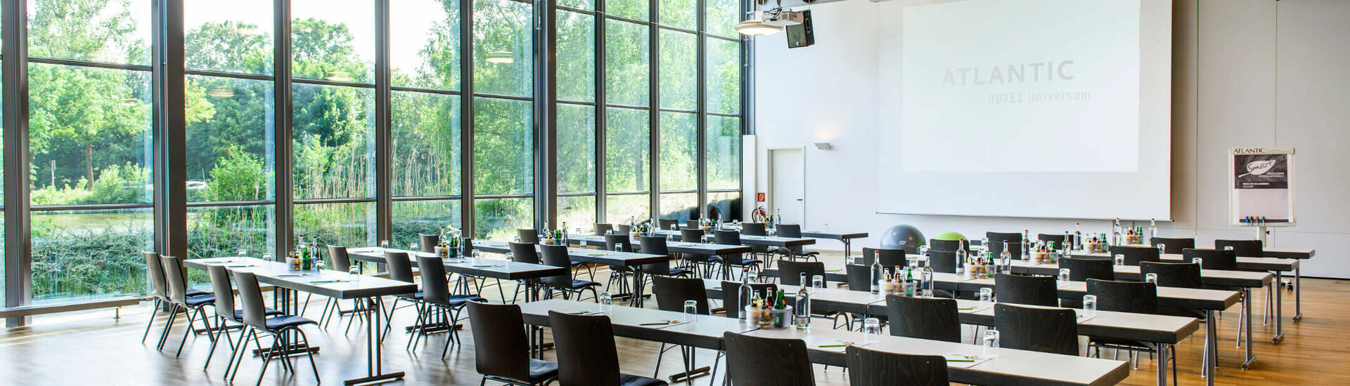 Heller Konferenzraum mit großen Fenstern, Tischen und Stühlen im ATLANTIC Hotel Universum Bremen.