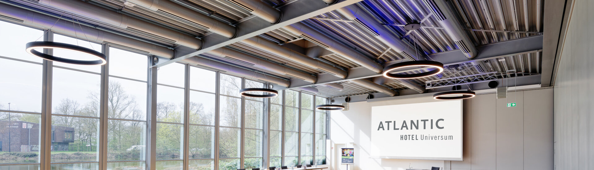 Bright conference room with large windows, tables and chairs at the ATLANTIC Hotel Universum Bremen.