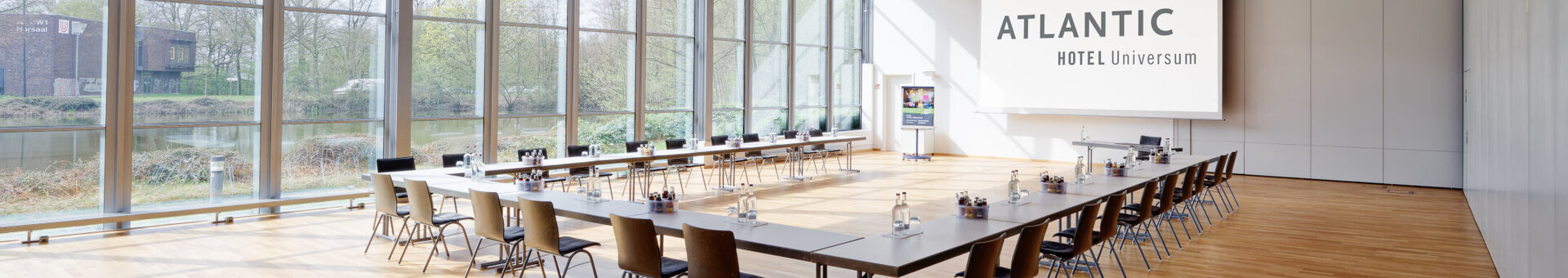 Heller Konferenzraum mit großen Fenstern, Tischen und Stühlen im ATLANTIC Hotel Universum Bremen.