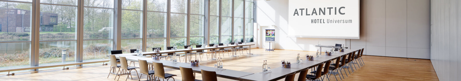 Bright conference room with large windows, tables and chairs at the ATLANTIC Hotel Universum Bremen.
