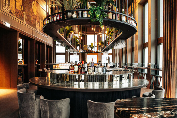 Moderne Hotelbar mit runder Theke, stilvoller Beleuchtung, Pflanzen und Spirituosenflaschen im ATLANTIC Hotel Heidelberg.