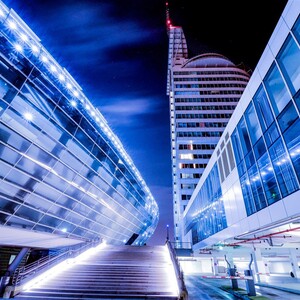 Night view of the ATLANTIC Hotel Sail City in Bremerhaven, illuminated with blue lights, modern design.