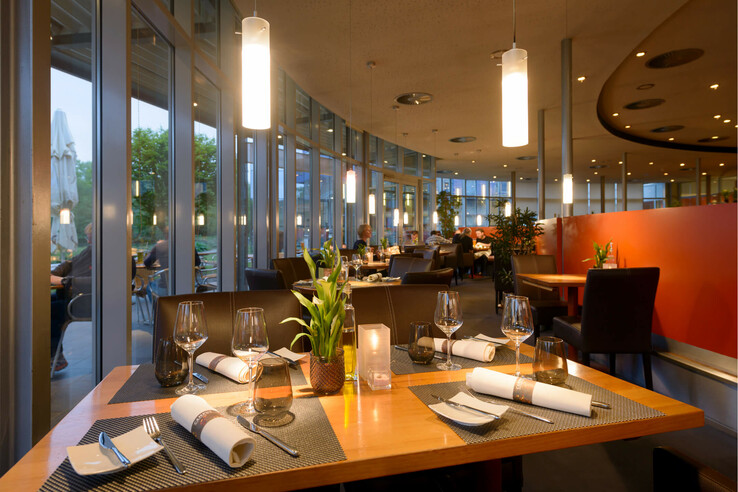 Modernes Hotelrestaurant mit elegant gedeckten Tischen, großen Fenstern und stimmungsvoller Beleuchtung im ATLANTIC Hotel Universum.