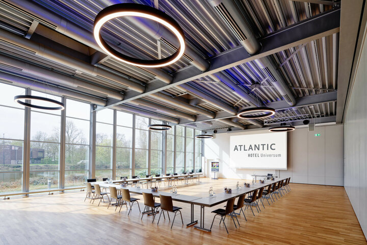 Moderner Konferenzraum im ATLANTIC Hotel Universum mit großen Fenstern, Holzboden und stilvollen Ringlichtern.