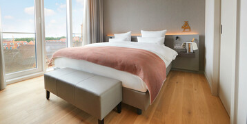 Bright hotel room with large bed, floor-to-ceiling windows and city view at the ATLANTIC Grand Hotel Bremen.
