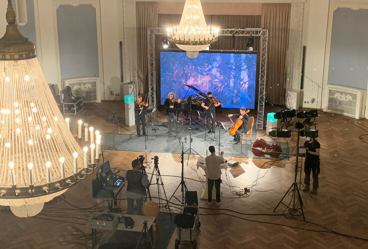 Konzert im ATLANTIC Grand Hotel Travemünde: Streicherensemble auf Bühne, beleuchtet von Kronleuchtern in elegantem Saal.