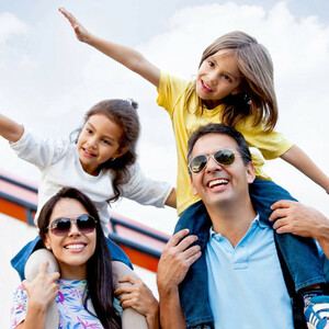 Family with two children happily outdoors, parents wearing sunglasses, children sitting on shoulders.
