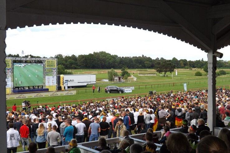 Zuschauer bei einem Event auf der Galopprennbahn Bremen, mit großer Leinwand und grüner Rennbahn im Hintergrund.