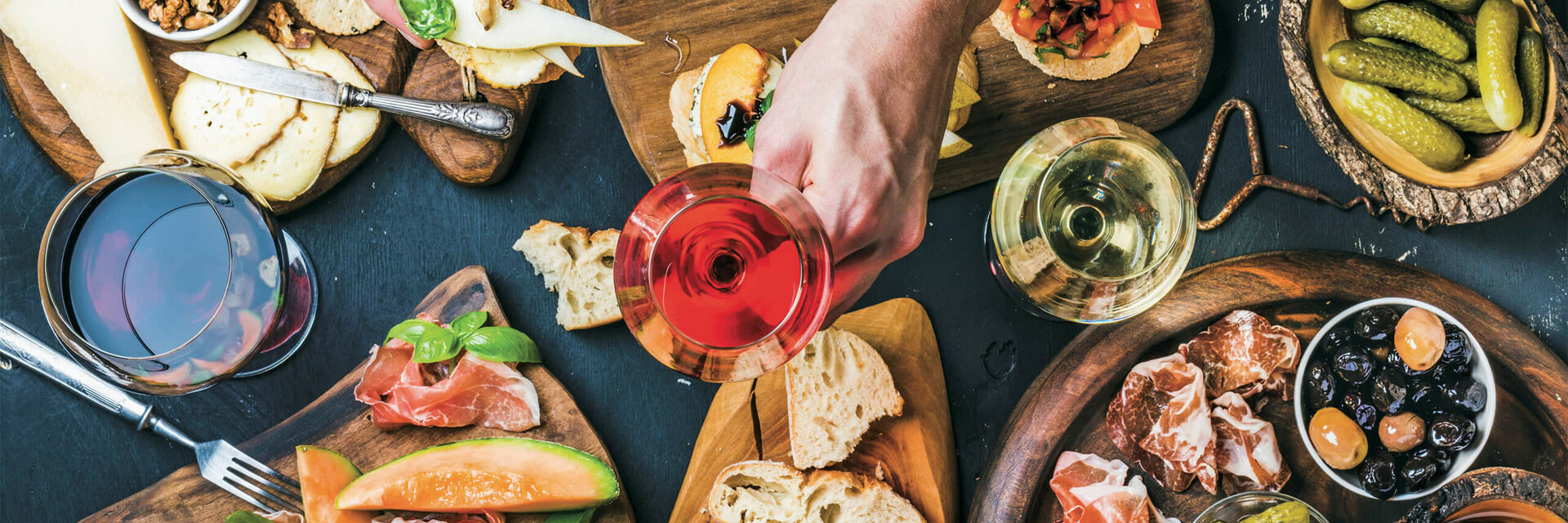 Various tapas with cheese, bread, ham, olives and wine glasses on wooden boards.