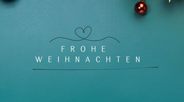 Weißer Text auf blauem Hintergrund: "Frohe Weihnachten", mit Tannenzweigen und Baumkugeln daneben.