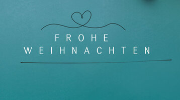 Weißer Text auf blauem Hintergrund: "Frohe Weihnachten", mit Tannenzweigen und Baumkugeln daneben.