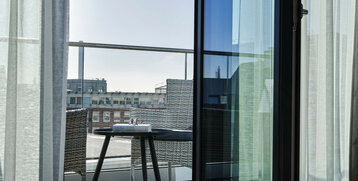 Blick von einem Hotelzimmerbalkon mit Glasgeländer, Tisch, zwei Stühlen und städtischer Aussicht im ATLANTIC Hotel Münster.