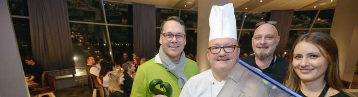 Gruppe von vier Personen im Restaurant, darunter ein Koch mit Abfallbehälter, lächeln in die Kamera.