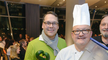 Group of four people in the restaurant, including a cook with a waste garbage can, smiling at the camera.