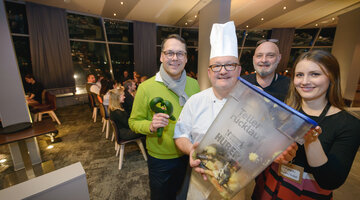 Gruppe von vier Personen im Restaurant, darunter ein Koch mit Abfallbehälter, lächeln in die Kamera.