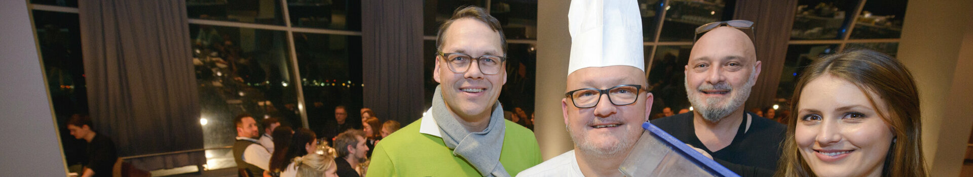 Group of four people in the restaurant, including a cook with a waste garbage can, smiling at the camera.