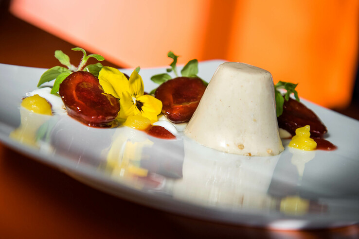 Elegantes Dessert mit Panna Cotta, gelben Blüten und Fruchtgarnitur auf weißem Teller im ATLANTIC Hotel Universum.