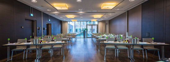 Moderner Konferenzraum im ATLANTIC Grand Hotel Bremen mit Tischen, Stühlen und Blick auf eine Fensterfront.