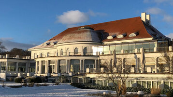 Historisches Gebäude des ATLANTIC Grand Hotel Travemünde, umgeben von schneebedecktem Garten unter blauem Himmel.