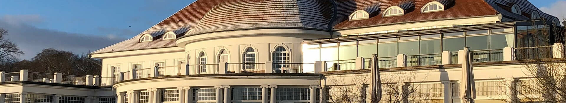 Historic building of the ATLANTIC Grand Hotel Travemünde, surrounded by a snow-covered garden under a blue sky.