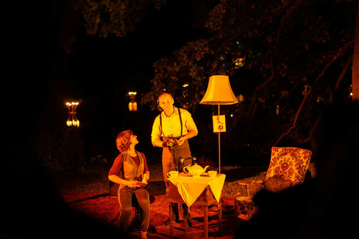 Gemütliche Abendstimmung mit zwei Personen, Tischlampe, Sessel und Teeservice im Freien.