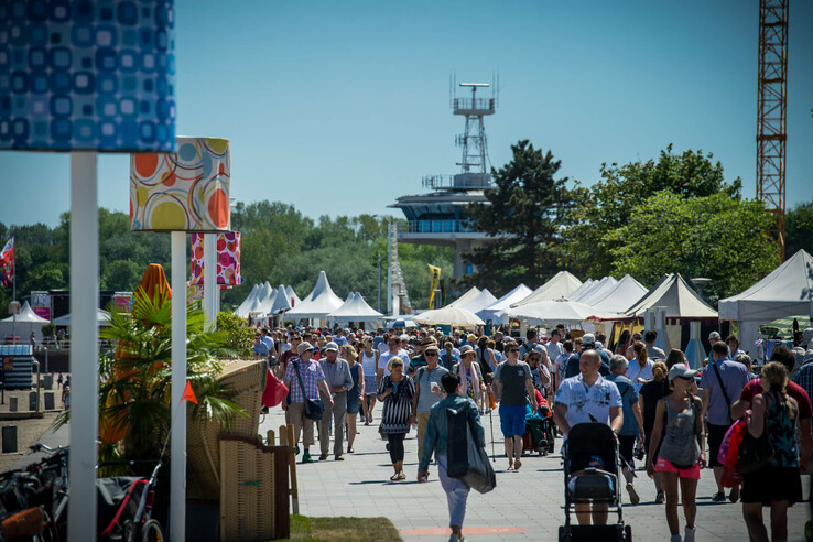 Belebte Strandpromenade in Travemünde mit vielen Menschen und bunten Marktständen bei sonnigem Wetter.