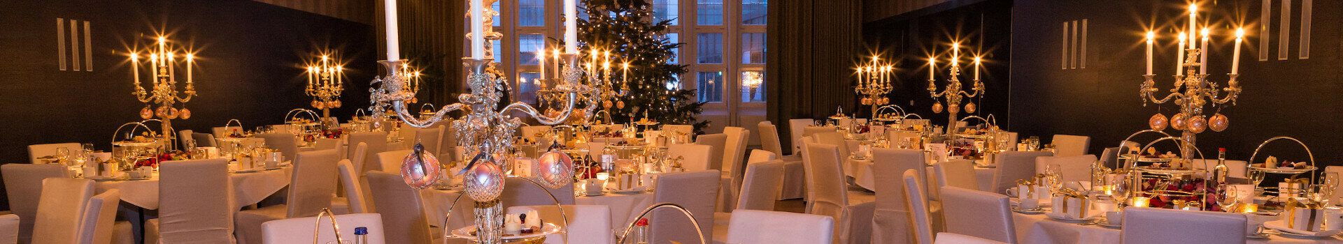 Elegantes Hotelrestaurant mit festlich gedeckten Tischen, Kerzenleuchtern und Weihnachtsbaum im Hintergrund.