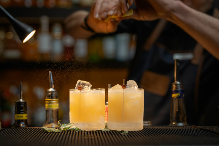 Two cocktails with ice cubes on a bar, a bartender refines them with citrus notes.