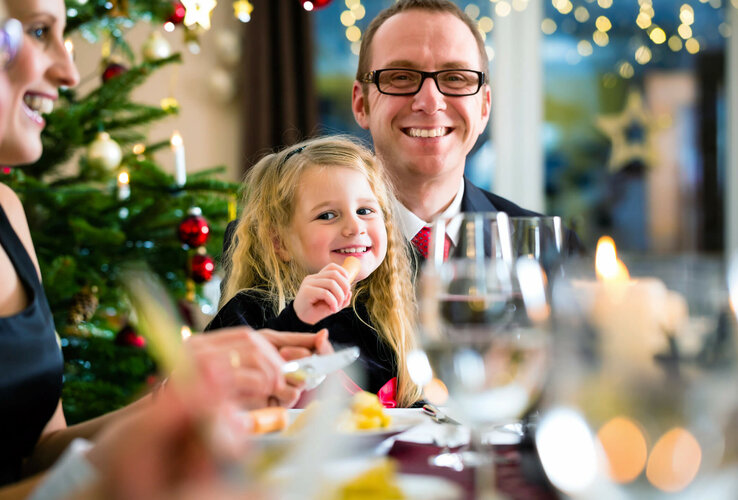 Family enjoying a festive dinner at the ATLANTIC Grand Hotel Travemünde, with Christmas tree in the background.