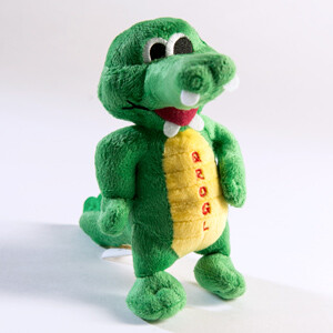 Kuscheltier "QROGL" das Krokodil Grünes Plüschkrokodil mit gelbem Bauch und roten Buchstaben, freundlich lächelnd.