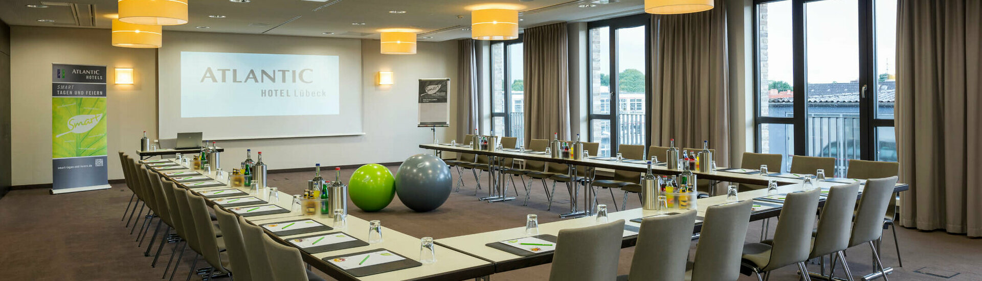 Modern conference room in the ATLANTIC Hotel Lübeck with U-shaped seating, projector and large windows.
