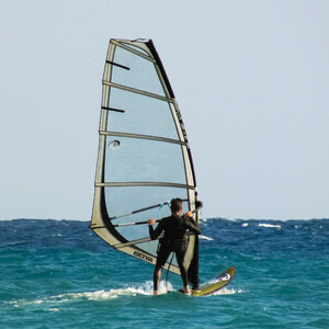 Person beim Windsurfen auf blauem Meer unter klarem Himmel.