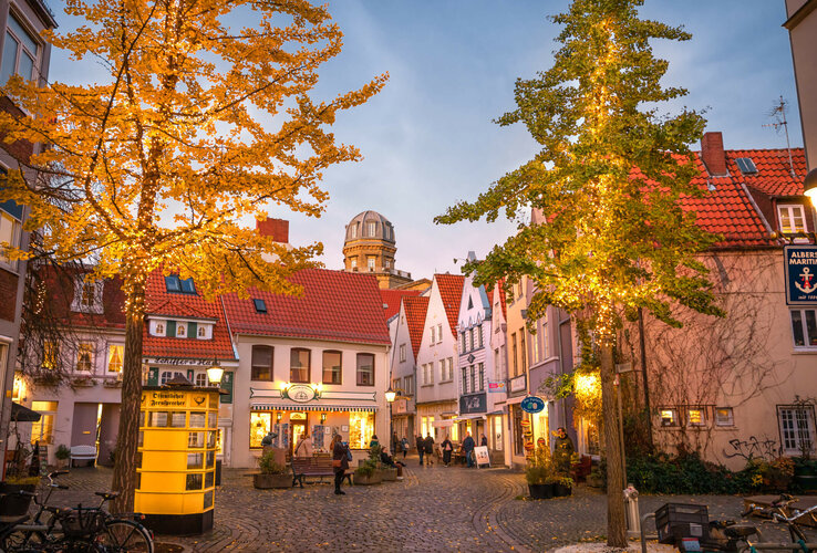 Illuminated square in Bremen's old town with half-timbered houses and autumnal trees, atmospherically lit up in the evening.