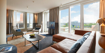Bright hotel room with leather sofa, armchairs, large window and city view at the ATLANTIC Grand Hotel Bremen.