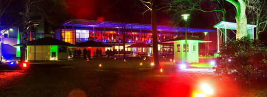 Beleuchteter Garten bei Nacht mit bunten Lichtern und moderner Architektur im Hintergrund.