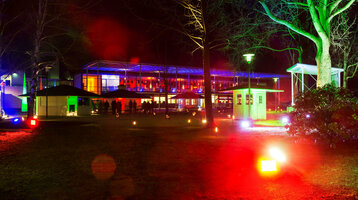 Beleuchteter Garten bei Nacht mit bunten Lichtern und moderner Architektur im Hintergrund.